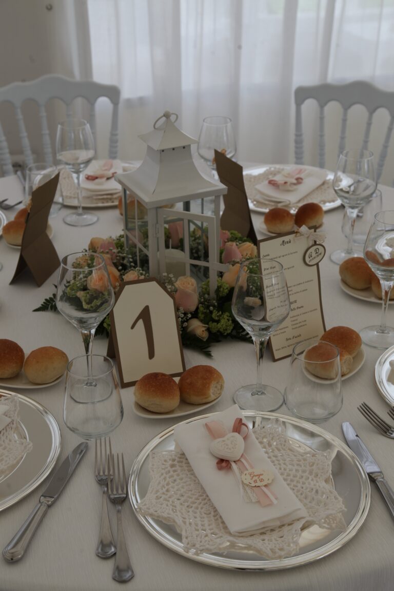 A place setting with a lace doily and heart charm beside a lantern centrepiece and table number, WEM Eventi