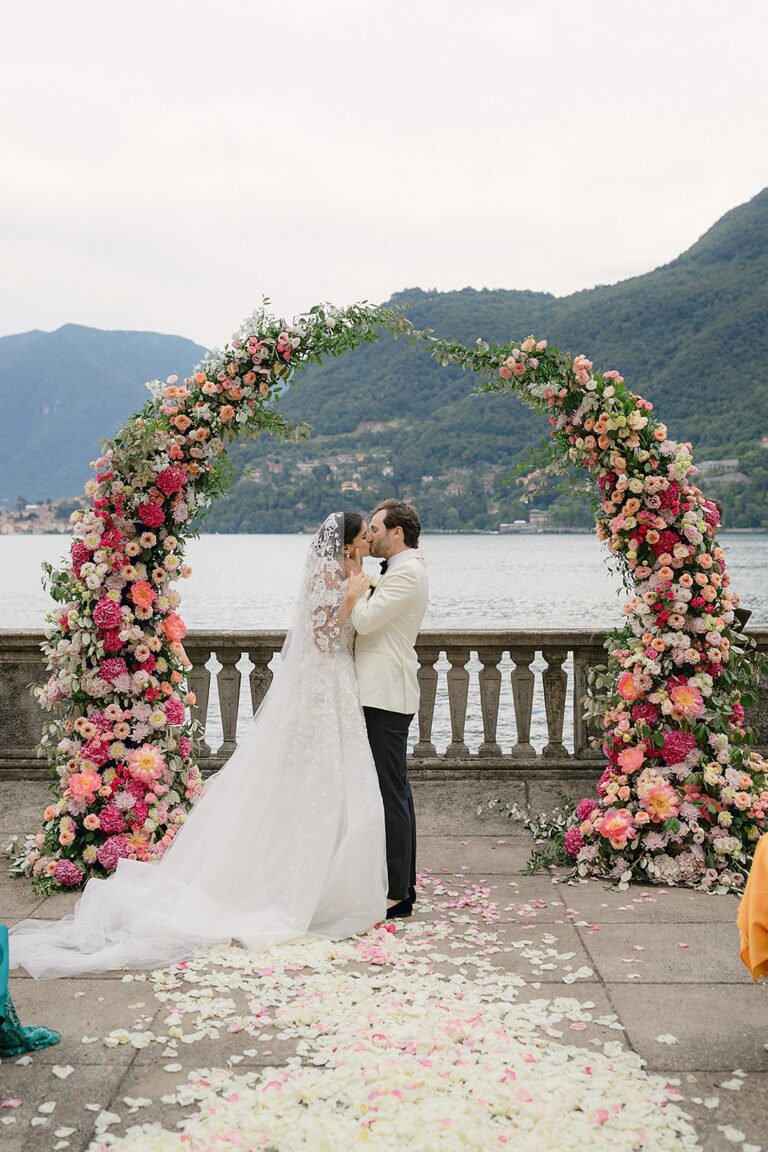 Natalie & Alex's kiss under a coral and pink floral arch above Lake Como, White Emotion