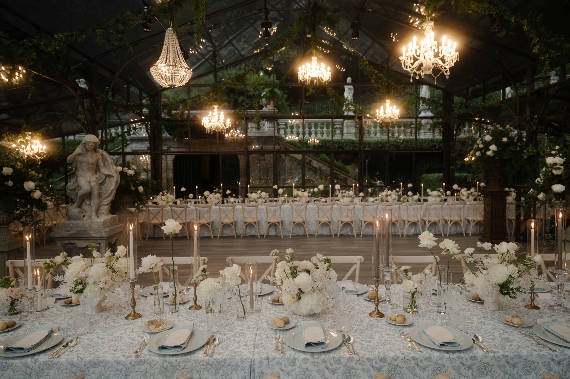 A glasshouse reception: chandeliers, a garden statue, a long dinner table dressed in blue and white, White Emotion