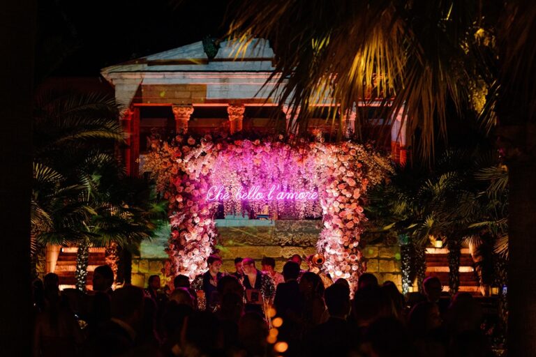 A night-time reception stage framed in pink flowers at a Sicilian villa, Whitesfilm Wedding Videography