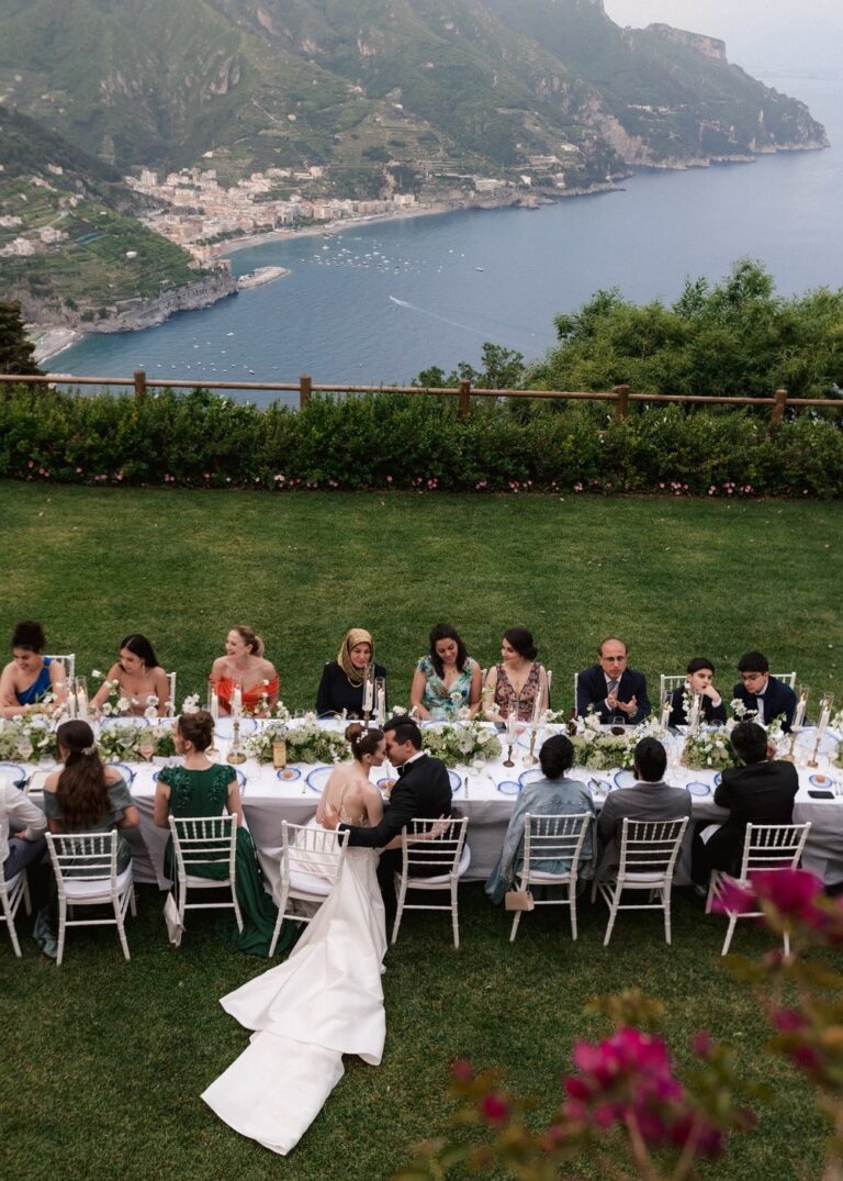 A bride passes the long table on the lawn at Villa La Rondinaia, Ravello, the coast below, Whitesfilm Wedding Videography
