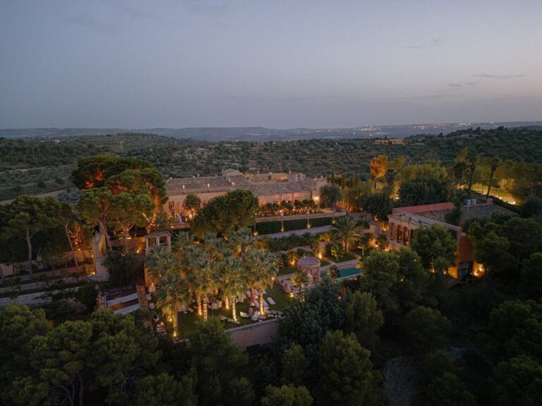 A Sicilian wedding estate lit up among palms and gardens at dusk, seen from the air, Whitesfilm Wedding Videography