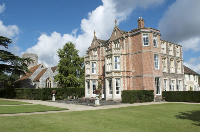 The red brick and stone front of the house from the lawn, with the flint church tower to the left, Wickham House