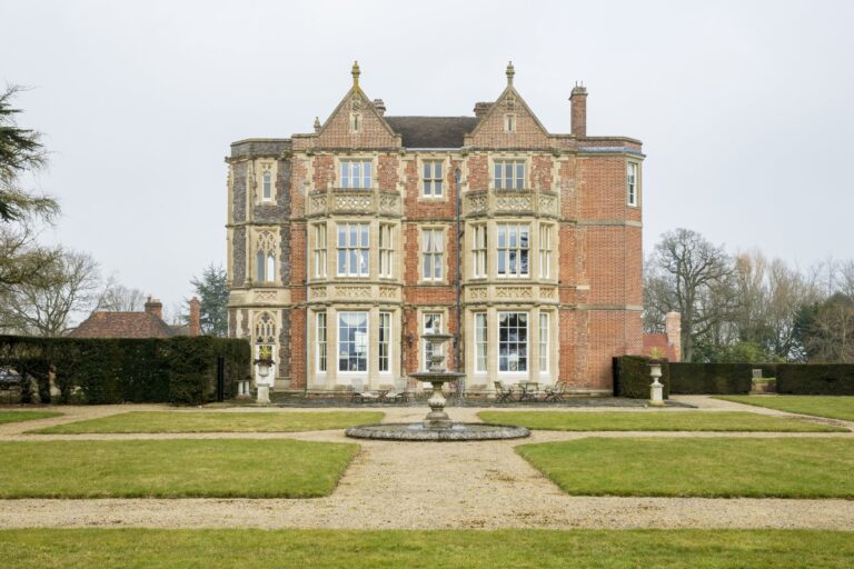 The main facade with its stone bay windows and gables, seen across the fountain and gravel walks, Wickham House
