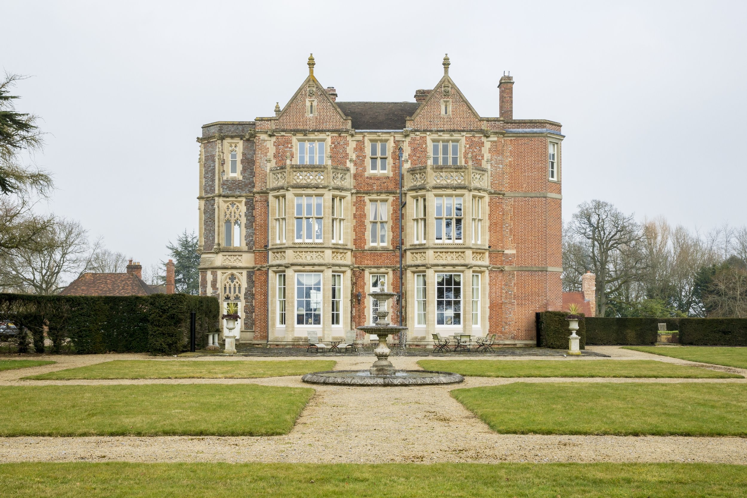 The main facade with its stone bay windows and gables, seen across the fountain and gravel walks, Wickham House
