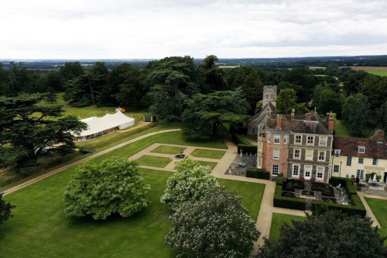A large marquee on the field in front of the house, seen from the air with the church and cedars, Wickham House