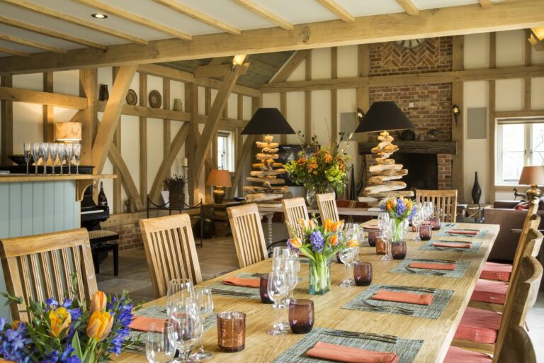 The oak-framed Barn with its dining table set with spring flowers and the fireplace behind, Wickham House