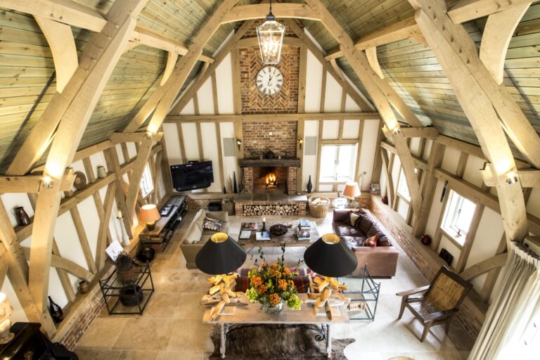 The Barn from the mezzanine: exposed oak trusses, the log fire, sofas and the dining table, Wickham House