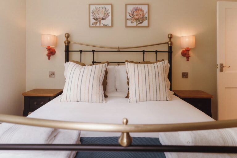 A bedroom at Gatehouse South with a brass bedstead, striped cushions and wall lights, Worstead Estate