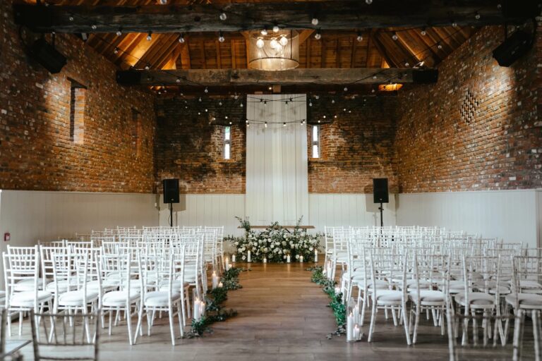 The Thatched Barn set for a ceremony, with rows of white chairs, a floral aisle and exposed brick walls under the timber roof, Worstead Estate