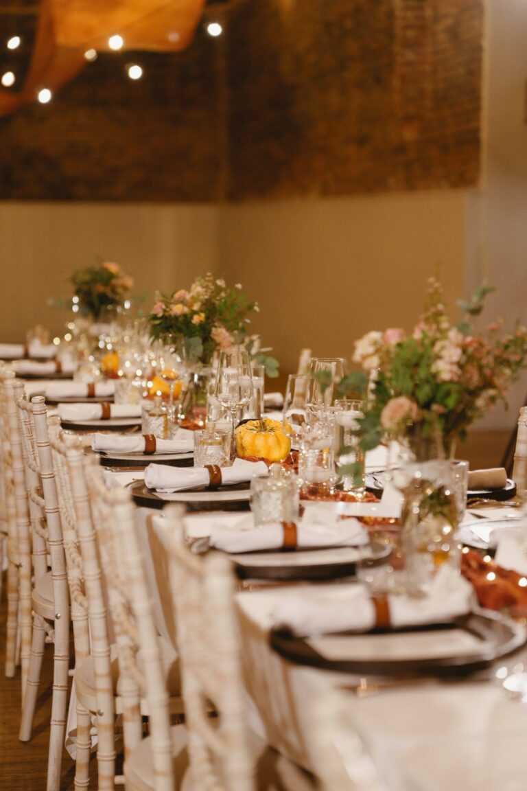 An autumn table setting with dried-flower arrangements, copper napkin rings and small pumpkins along a long table in the barn, Worstead Estate