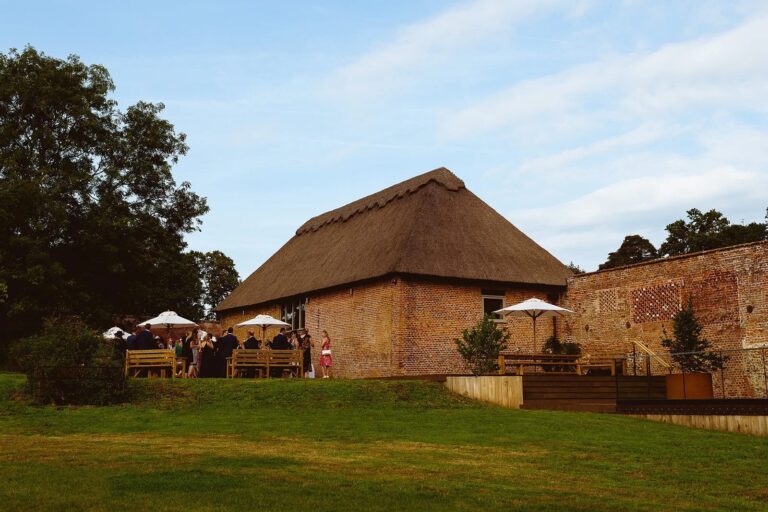 Guests on the West Terrace beside the thatched barn and the old brick wall, with the lawn sloping away in front, Worstead Estate