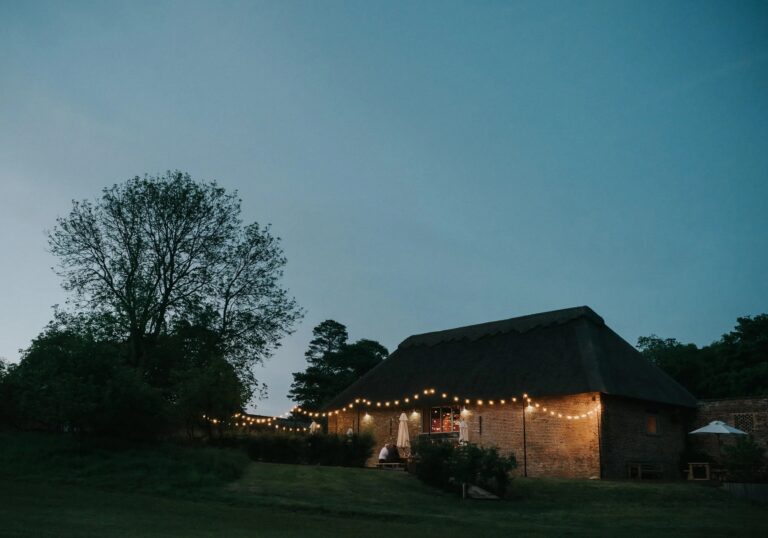 The thatched barn at dusk with festoon lights strung along the terrace, Worstead Estate