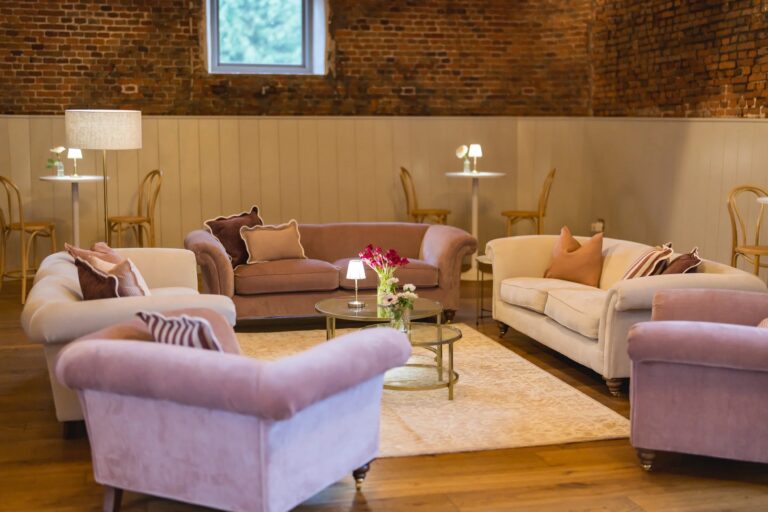 A lounge area in the Thatched Barn with velvet sofas, side tables and lamps against brick and panelled walls, Worstead Estate