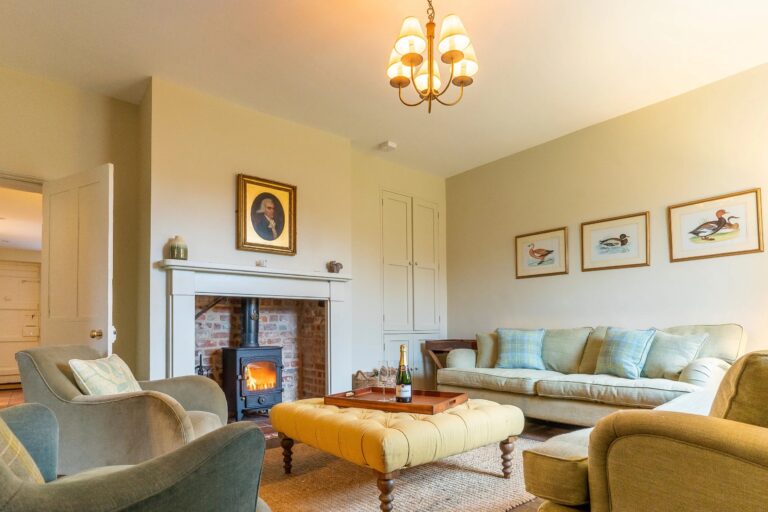 The sitting room at Estate Cottage with a wood-burning stove, a yellow footstool and sofas in pale green, Worstead Estate