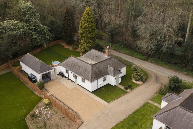 Gatehouse South from the air, a single-storey white lodge with its garden, hot tub and the park drive alongside, Worstead Estate