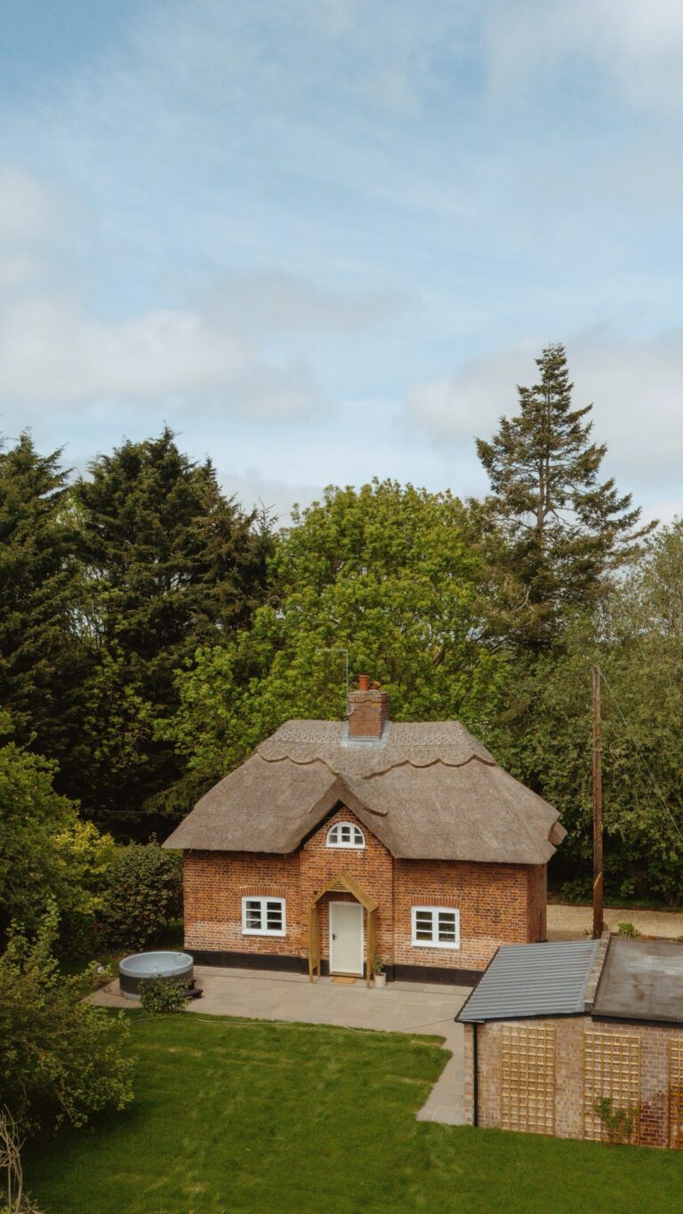 Swann Cottage, thatched and in brick, with its lawn, terrace and hot tub, seen from above the garden, Worstead Estate