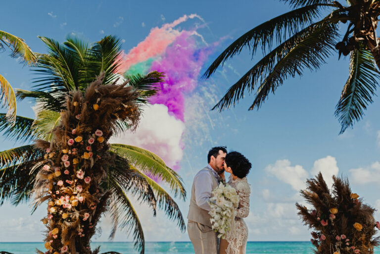 A couple kiss among palms as coloured smoke drifts behind them, YD Events