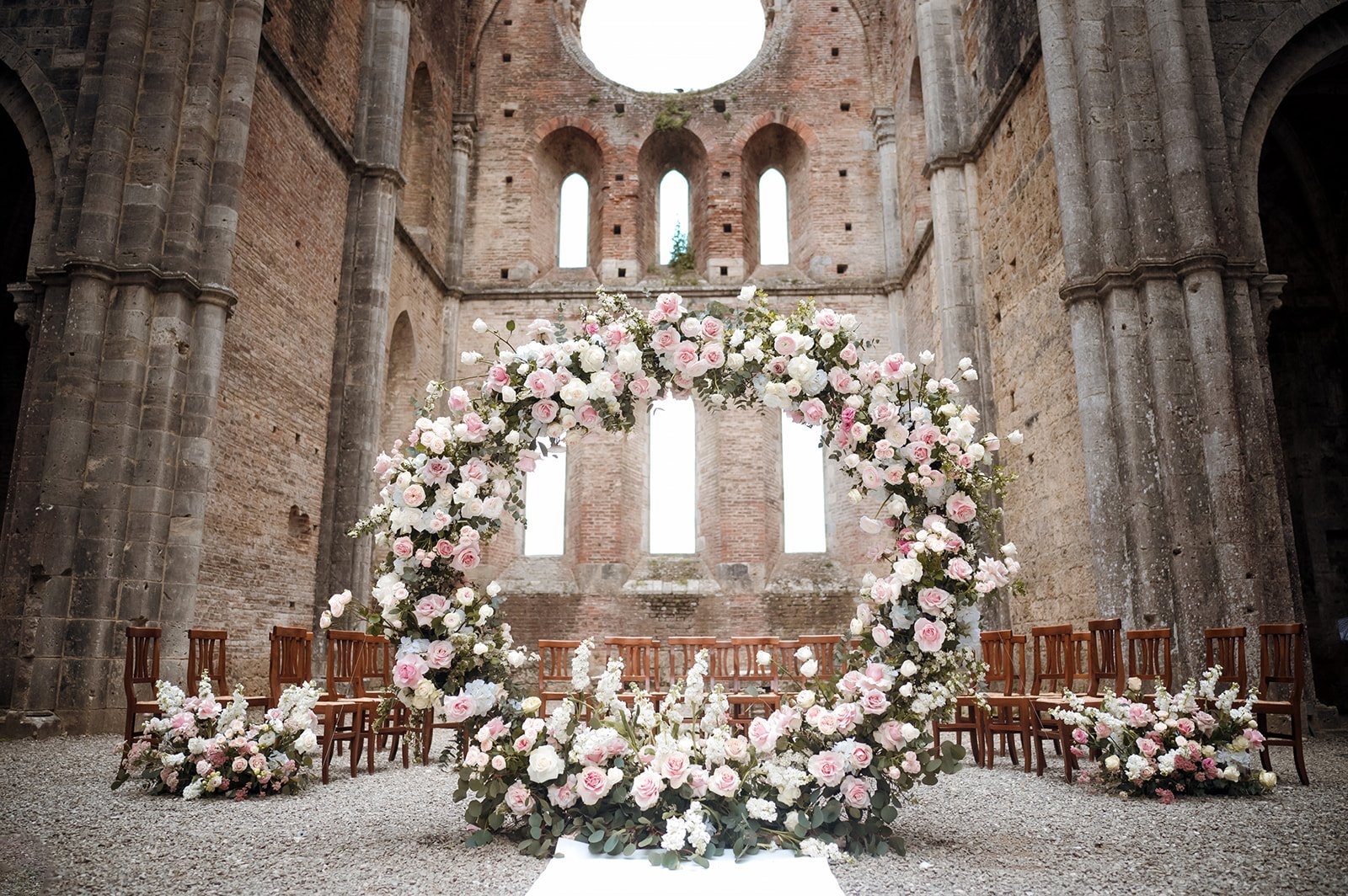 A circular arch of pink and white roses inside the roofless nave of San Galgano Abbey, Siena, Your Secret Tuscany