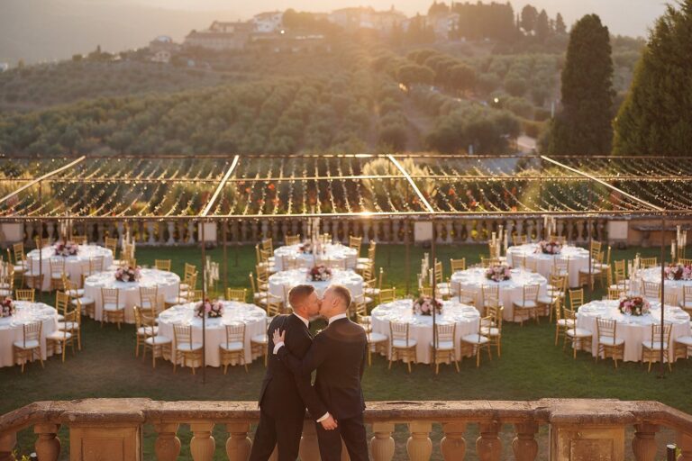 Two grooms kissing at golden hour above a dressed reception lawn at Tenuta di Artimino, Florence, Your Secret Tuscany