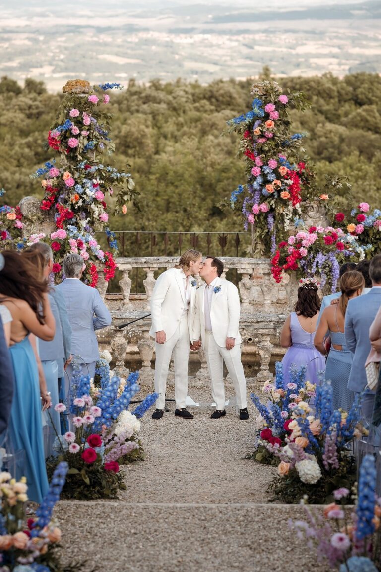 Two grooms kissing on a Castello di Celsa terrace, floral installations either side, the Tuscan valley below, Your Secret Tuscany