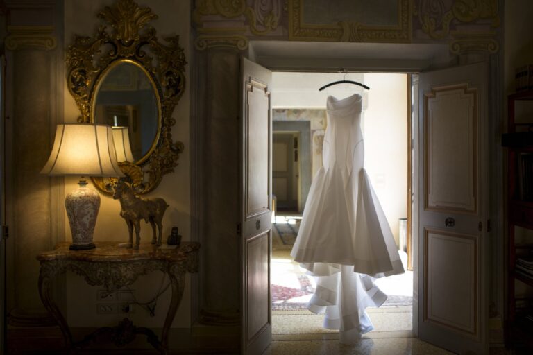 A wedding dress on a hanger, backlit in an open doorway between two frescoed rooms, Your Secret Tuscany