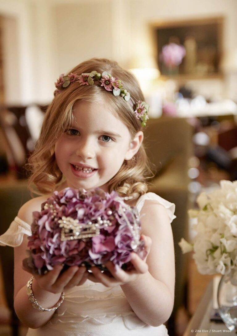 A flower girl in a floral crown, holding a hydrangea-covered bag, Zita Elze
